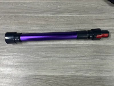 A purple extension tube for a vacuum cleaner is laid horizontally on a wooden floor.