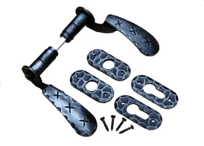A set of antique black wrought iron door handles and escutcheon plates with screws, laid out on a white background.