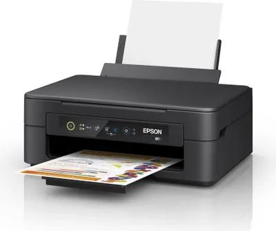A black Epson Expression Home XP-2205 printer is shown from a slightly elevated front-left angle, with a sheet of paper partially printed with colorful graphics emerging from the output tray and a blank sheet of paper in the input tray.