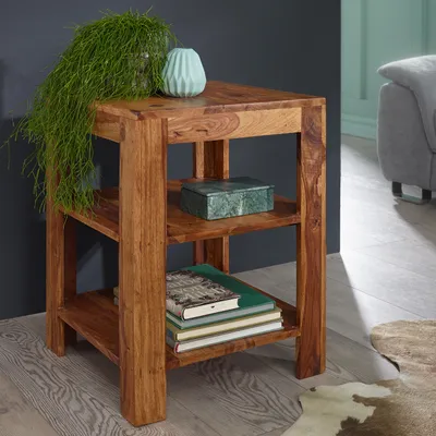 A wooden side table with shelves, decorated with a plant, a vase, a decorative box, and books, placed in a living room setting.