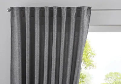 A close-up view of a gray curtain hanging from a rod, with a window and trees visible in the background.