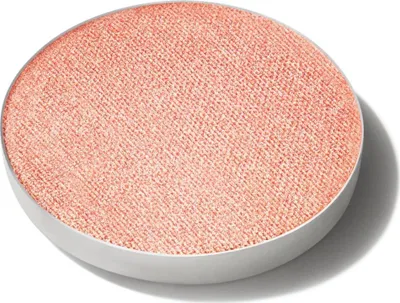 A close-up, top-down view of a single round eyeshadow pan with a shimmery peach-pink color.