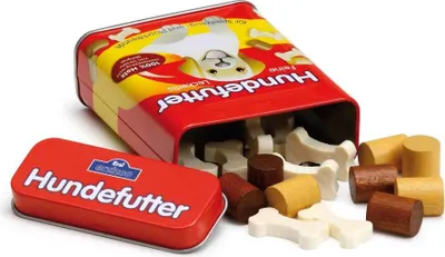 A red tin of wooden dog treats, with some treats spilled out onto a white surface.