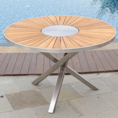 A round teak wood table with a metal base sits on a patio next to a swimming pool.