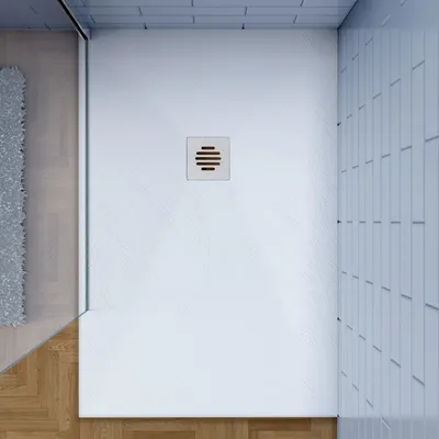 A top-down view of a white shower tray with a drain in the center, adjacent to a wooden floor and a grey rug.