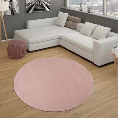 A pink round rug is placed on a wooden floor in front of a white sectional sofa in a modern living room.