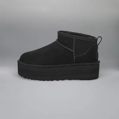 A black UGG boot with a platform sole is shown against a plain gray background.