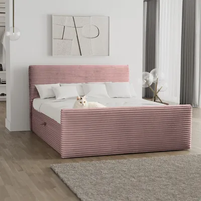 A pink upholstered bed with white pillows and a white cat lying on it, in a bedroom setting with artwork on the wall and curtains in the background.