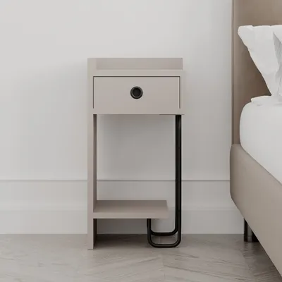 A modern nightstand with a drawer and an open shelf, placed next to a bed in a bedroom setting. The nightstand has a light mocha finish and black metal legs.