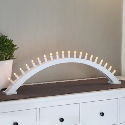 A white arched candle lamp with 20 lights sits on a white dresser, with a potted plant to the left.
