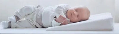 A newborn baby sleeping on an inclined wedge pillow.