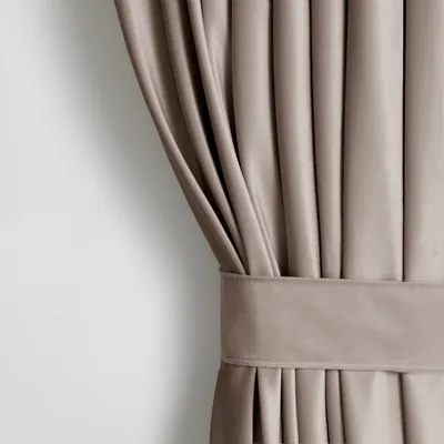 A close-up view of a beige velvet curtain with pleats and a tie-back.