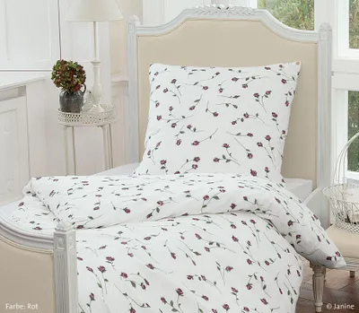 A close-up view of a bed with white bedding featuring a red floral pattern.