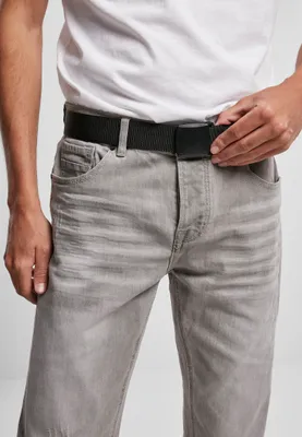 A person wearing a white t-shirt and grey jeans, adjusting a black belt.