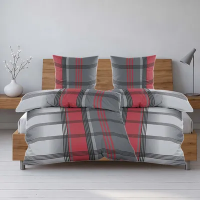 A neatly made bed with a red, gray, and black plaid duvet cover and matching pillowcases, set against a wooden headboard and a white wall.