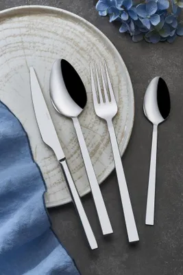 A set of cutlery laid out on a plate with a blue napkin and blue flowers in the background.