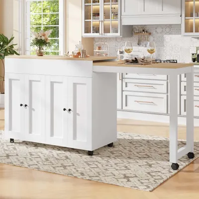 A white kitchen island with a wooden countertop is shown in a well-lit kitchen. The island has four cabinet doors and a pull-out table extension. Two wine glasses and some tableware are placed on the extended table.