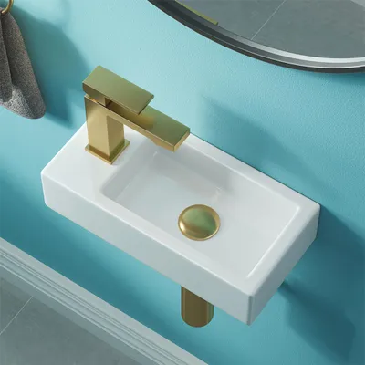 A close-up view of a small white sink with a gold faucet mounted on a blue wall.