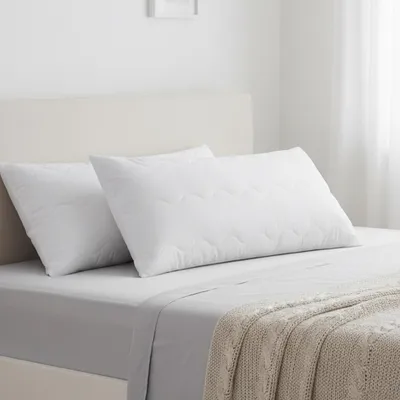 Two white pillows on a bed with a light-colored headboard and a knitted throw blanket.
