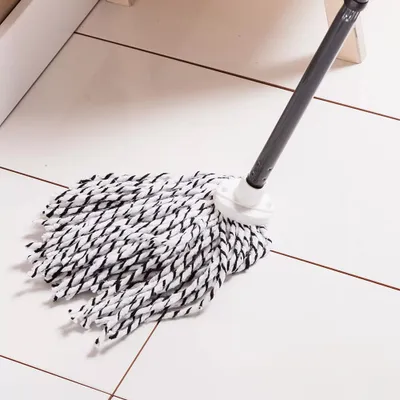 A mop head with black and white strands rests on a tiled floor.