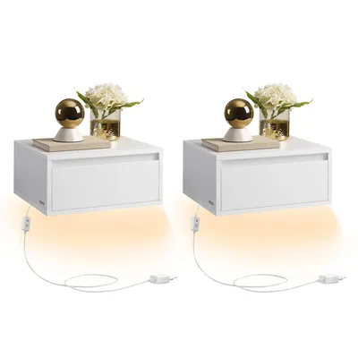 Two white floating nightstands are displayed against a white background. Each nightstand has a drawer and is decorated with a book, a golden orb lamp, and a vase of white flowers. LED lights beneath the nightstands cast an orange glow.