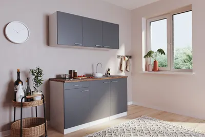 A small kitchen unit with upper cabinets, a sink, and countertop, set against a wall with a window.