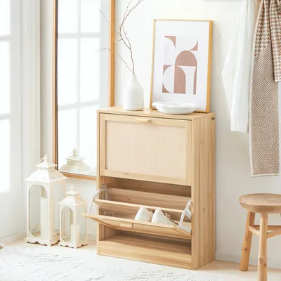 A wooden shoe cabinet with two flip-down drawers is shown in a hallway next to a mirror and a stool. The cabinet is filled with shoes, and decorative items like lanterns and a vase with branches are placed around it.