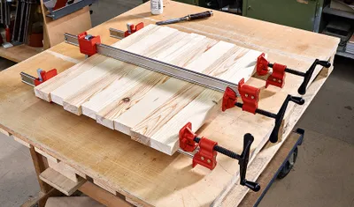 A woodworking clamp is holding together several pieces of wood on a workbench.