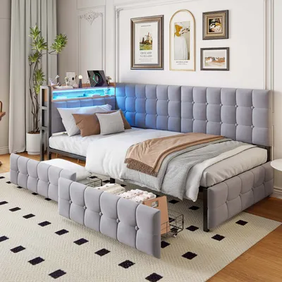 A modern bedroom with a grey upholstered daybed featuring built-in LED lighting and storage drawers. The bed is made up with pillows and a throw blanket.