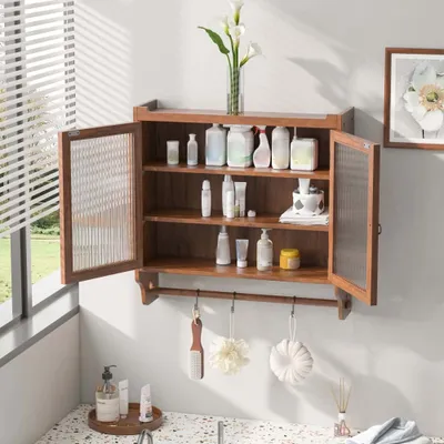 A wooden wall-mounted cabinet with glass doors, filled with various bathroom products, is shown in a well-lit room with a window.