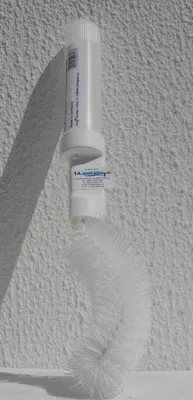 A white toilet brush with a liquid dispenser attached, leaning against a textured white wall.