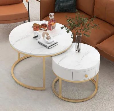 A set of two round nesting coffee tables with marble-like tops and gold metal legs, placed on a rug next to a brown leather sofa.
