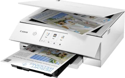 A white Canon PIXMA TS8351a 3-in-1 inkjet multifunction printer is shown from a diagonal front view. The scanner lid is open, revealing paper inside. A printed document is exiting the paper tray.