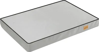 A light gray dog bed with black piping around the edges, shown from a slightly elevated angle on a white background. A small, light brown tag with text is visible on the right side of the bed.