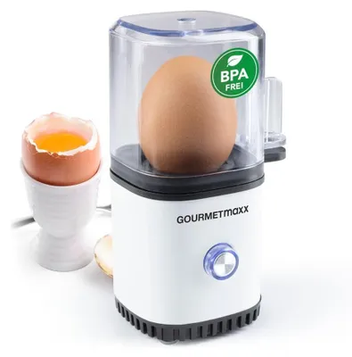 A Gourmetmaxx egg cooker with an egg inside, next to a soft-boiled egg in an egg cup.