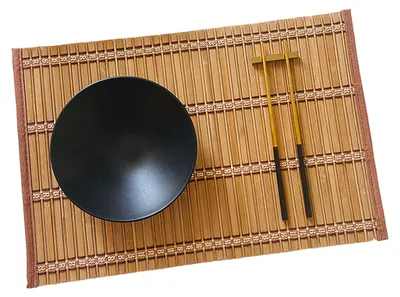 A black bowl and chopsticks are placed on a bamboo placemat.