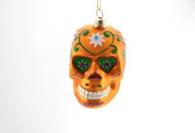 A single orange sugar skull ornament hangs from a gold string against a white background.