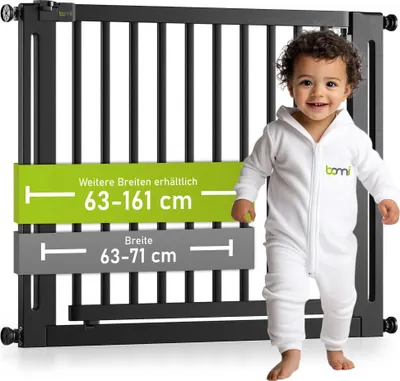 A baby in a white onesie stands next to a black safety gate with size information displayed.
