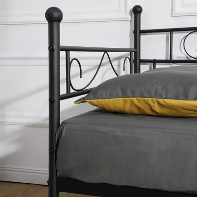 Close-up of a black metal bed frame with bedding and a pillow.