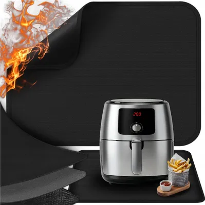 A black heat-resistant mat with flames in the corner, an air fryer, and a basket of french fries on a wooden board.