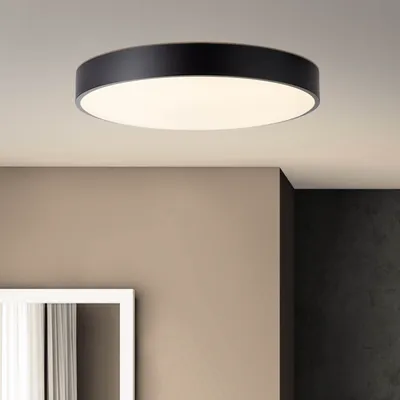 A modern black and white ceiling light fixture is shown mounted on a white ceiling, with a wall and a mirror visible in the background.