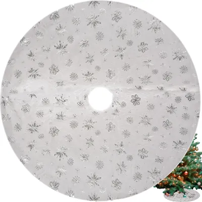 A white circular Christmas tree skirt with silver snowflake patterns is shown, with a portion of a decorated Christmas tree visible in the bottom right corner.
