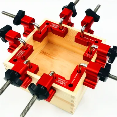 A set of red corner clamps is attached to a wooden box, demonstrating their use in woodworking.