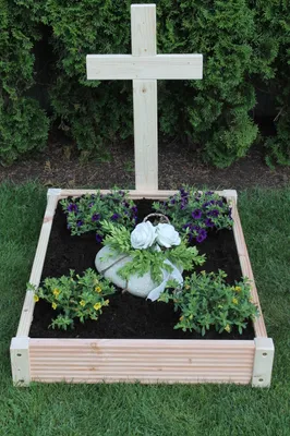 A wooden grave border with a cross and flowers.