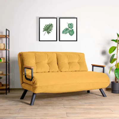 A yellow sofa is shown in a room with two framed pictures of leaves on the wall and a plant in a pot.