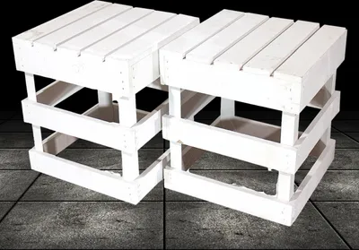 Two white wooden stools with a slatted top and a slatted base, placed on a tiled floor with a dark background.