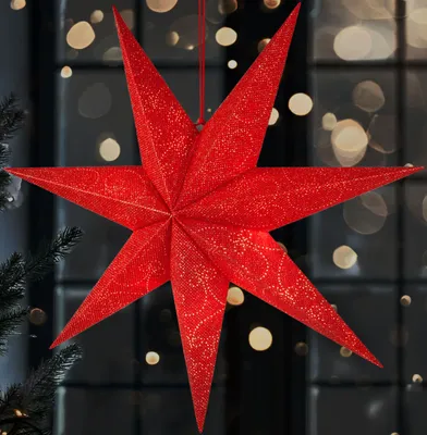 A red star-shaped Christmas decoration hangs in front of a window with bokeh lights.