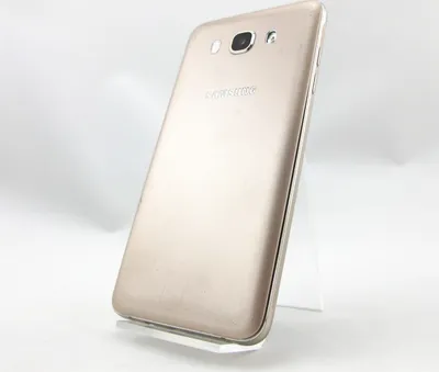 A gold Samsung Galaxy J7 (2016) smartphone is displayed on a clear stand against a white background.