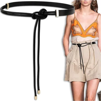 A black leather belt with gold accents and a knot detail is shown on a model wearing a beige outfit.