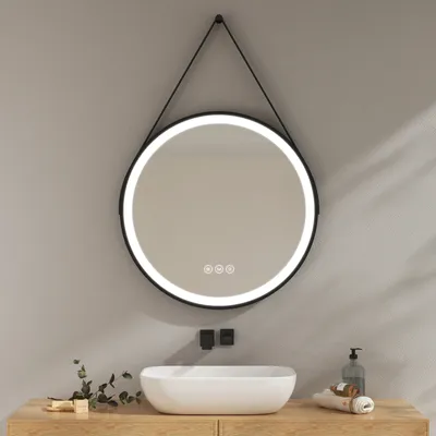 A round LED mirror with a black frame hangs above a white sink on a wooden vanity. The mirror has a built-in light and touch controls.
